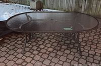 Oval patio table with textured glass top and metal frame outdoors on paved surface