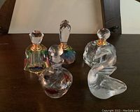 Four glass perfume bottles with stoppers and one glass swan figurine arranged on a wooden surface.