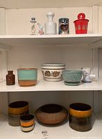 Three shelves displaying ceramics, Raku pottery, porcelain, and some metalware including MCM style from Germany.