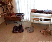Photo shows a variety of bags on a small table and white shelving against a bright window with sheer curtains. Several bags are brown leather, one is multicolored patchwork, and there is a colorful fabric handbag.