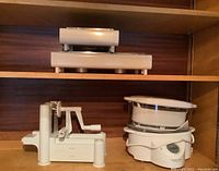 Image showing mandolin slicer, two Brabantia food warmers stacked, and Black & Decker floor steamer on wooden shelf.