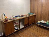 Wide shot of wooden cabinet in basement with assortment of tools and hardware laid out on top and nearby bench.
