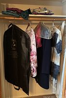Photo showing several garments hanging in a closet including a garment bag and various blouses and tops.