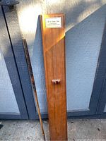 Full view of the antique hickory shaft golf putter leaning next to the wooden St. Andrews putter wall display with mounted plaque and putter holder.