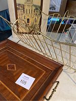 Photo showing brass magazine holder and wood inlay serving tray on wooden surface with framed artwork in background