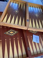Two foldable wooden game boards, one is a backgammon set showing hinged fold, distinctive triangular points, and inlay design in center. The other board partially visible underneath.