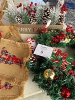 Photo showing burlap Merry Christmas banner with plaid patches, wooden planter box filled with frosted pinecones, pine branches, red berries, and small trees as holiday decorations
