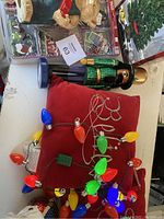 Image showing nutcracker figurine, red pillows, colorful string lights, and boxes of gift tags, with a boxed talking Christmas tree in background.