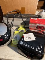 Box with electronic items including two CD players, paper shredder top, two red LED alarm clocks, and a cable in its package.