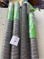 Four rolls of galvanized poultry netting laid out on table. Three rolls wrapped in green plastic with labels confirming 3ft x 25ft size for three rolls and 2ft x 25ft for one roll; one roll is unwrapped.