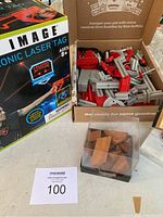 Photo showing Sharper Image electronic laser tag box, erector set parts in an open box, and wooden puzzle pieces in a clear cube