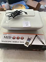 HP DeskJet 2540 printer and power adapter placed on top of Neewer telescopic mobile rack box.