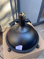 Black industrial nautical pendant ceiling light laying on cardboard with visible mounting arms, cylindrical pipe on top, missing ceiling hook.