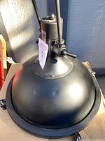 Top view showing black dome-shaped metal shade with mounting bracket and hanging mechanism, showing minor surface imperfections.