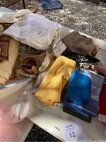Various scarves, handkerchiefs, and linens stacked together showing embroidered cream fabric, yellow scarf, and blue-striped cloth.