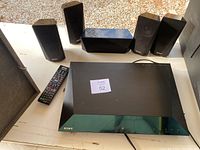 Top-down view of Sony Blu-Ray player with all five speakers and remote control on white surface.