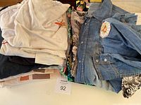 Stack of folded men's t-shirts and shirts including a denim shirt with patch.