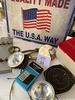 Photo showing vintage items including metal Radio Compass, handheld flashlights, blue Sharp calculator, convex mirrors, and metal sign with American flag