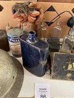 Blue enamel canteen, Purex flax linen tea tin, some glass bottles, wood-carved troll figurine visible, vintage helmet edge visible