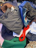 Pile of mens and womens vintage clothing in various colors and fabric textures, including blazers and scarves.