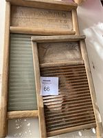 Two vintage wooden washboards lying side by side on a white surface. One washboard has a glass wash surface with 'Atlantic National Washboard Co' text visible on the wood frame. The other washboard shows a ribbed metal wash surface and faded labeling 'Lingerie.'