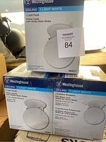 Photo showing boxes of three Westinghouse 1 Light White ceiling lights, model 66607, with white glass globes and flush mount design.