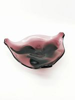 Angled view of an amethyst-hued art glass bowl showing smooth, wavy edges and blemishes.