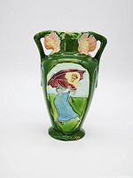 Front view showing green Majolica vase with woman holding umbrella in blue dress and yellow bonnet, two pink flowers near the dual handles.