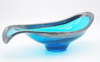 Blue art glass bowl with silver overlay rim resting on white background, showing the asymmetrical elongated oval shape with one curling end.