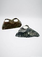 Two carved soapstone candle holders positioned on a plain surface, one brown with visible wear and chips, the other grey and smoother in finish.