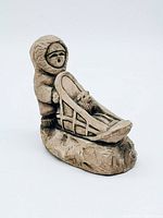 Side angle view of the handcrafted Earthquake Clay Inuit sculpture showing the figure standing behind a sled carrying a small dog or animal figure, on a textured base.