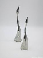Both aluminum crane sculptures together, showing their relative sizes and polished finish
