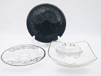 Lot of 3 silver overlay glass pieces including a black glass plate on stand, a clear glass plate, and a square-shaped clear glass bowl with floral silver overlay decoration.