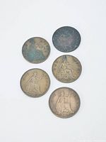 Five vintage British pennies laid out with obverse and reverse sides visible, showing monarch portraits and seated Britannia designs.
