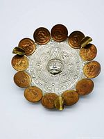Top-down view of vintage ashtray showing central Mayan calendar design surrounded by 12 Mexican coins and 3 coin holders.
