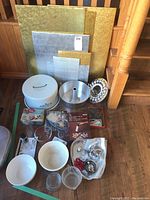 Full overview of all bakeware items on wooden floor showing pudding bowls, metal cake carrier, cookie cutters, measuring cups, cake boards, and smaller baking tools.