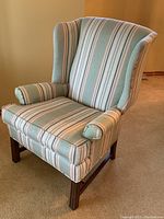 Front angled view of upholstered wing chair showing striped fabric, removable seat cushion, and wooden legs.