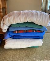 Stack of 4 folded blankets showing various colors and fabrics including white, blue, and green