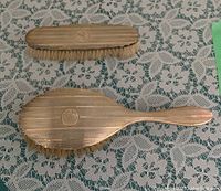 Two-piece sterling silver brush set with monogram 'R' and linear textured design on lace background.