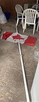 Full view of flagpole lying on ground attached to Canadian flag, showing overall length, pulley system, and rope.