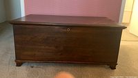 Front view of the closed wooden blanket chest showing dark wood finish and brass keyhole.