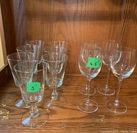 Photo showing 7 cordial glasses on the left measuring approx. 5 inches and 4 crystal glasses on the right measuring approx. 6.5 inches placed on a wooden surface.