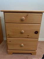 Front view of the small pine wood dresser showing three drawers with round wooden knobs and natural pine wood grain and knots.