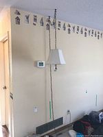 Swag lamp hanging from ceiling with white fabric shade and metal chain visible. Partial wall decor and thermostat in view.