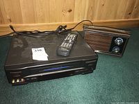 Panasonic VHS player with a remote control on top and North Star portable radio next to it on a green carpet with wooden panel wall background.