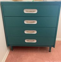 Front view showing four drawers with white recessed panels and brass metal drawer pulls on a teal painted dresser.