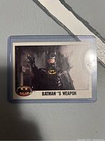 Front of the trading card showing Batman aiming a weapon with 'BATMAN'S WEAPON' text and Batman logo.