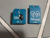Front view of the boxes showing the keychain case and silicone ear hooks for Apple AirPods.