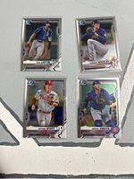 Front sides of four Bowman Chrome 2021 baseball cards: Nick Loftin, Forrest Whitley, Bryson Stott, Miguel Amaya, arranged in a square on grey surface.