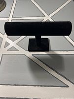 Black felt jewelry display stand on a gray patterned surface.